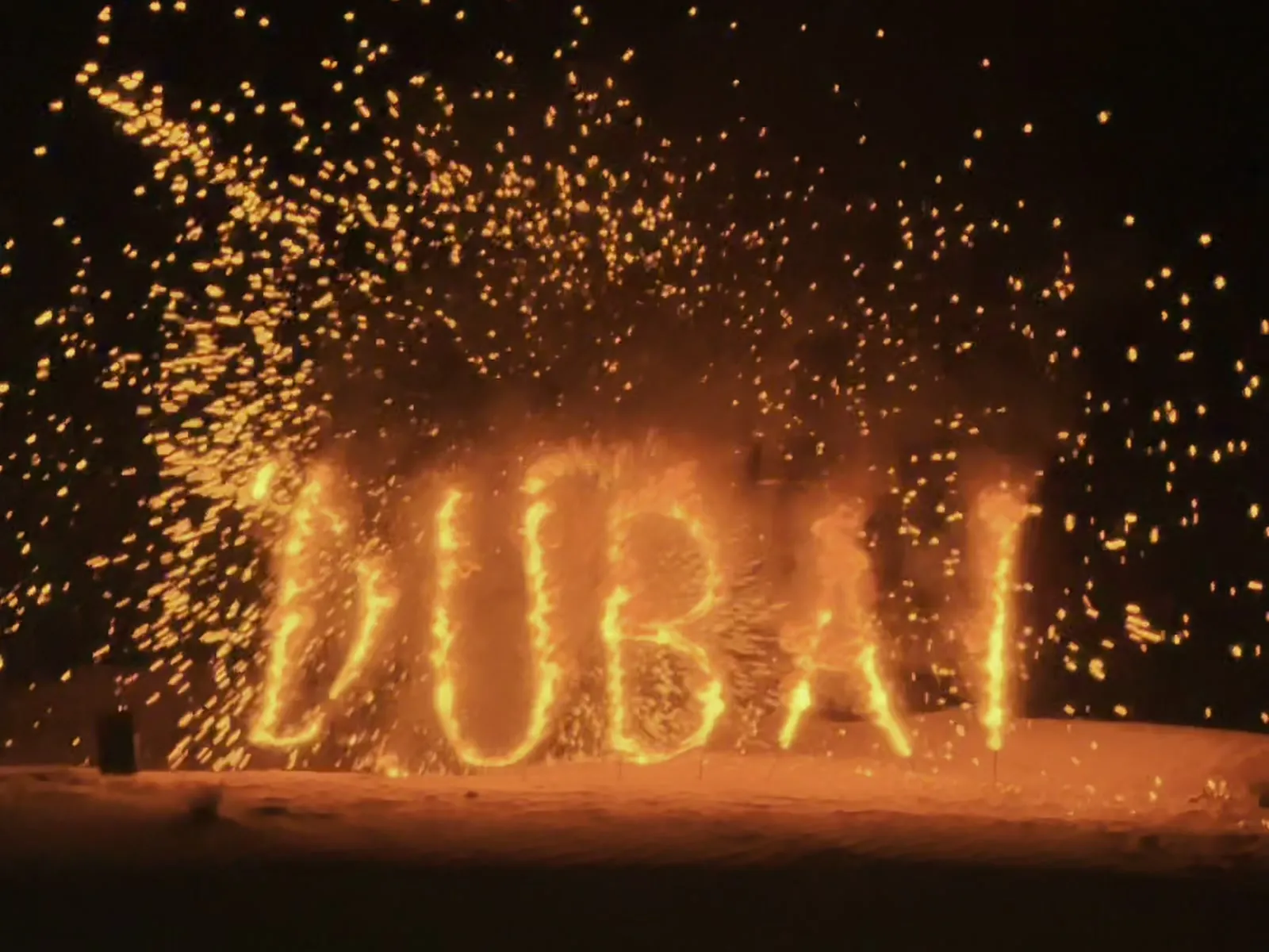The word DUBAI burning in letters of fire on the sand at night